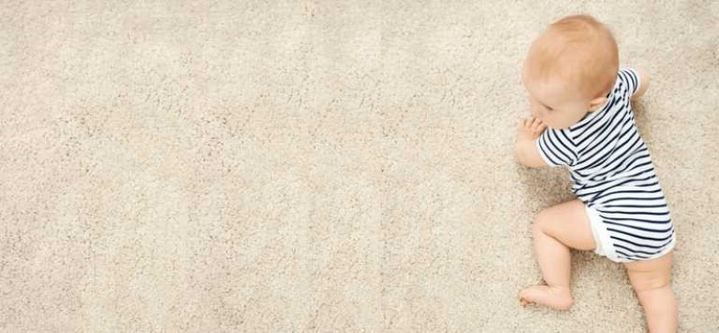 Manos aplicando una solución diluida de jabón para platos Dawn en una mancha de aceite en una alfombra sintética utilizando una botella rociadora y un cepillo de cerdas suaves.